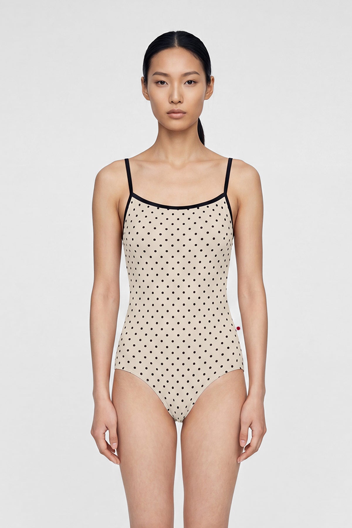 AI-generated model. Daniela leotard, all-over cream polka-dot with thin black straps and black neckline trim.