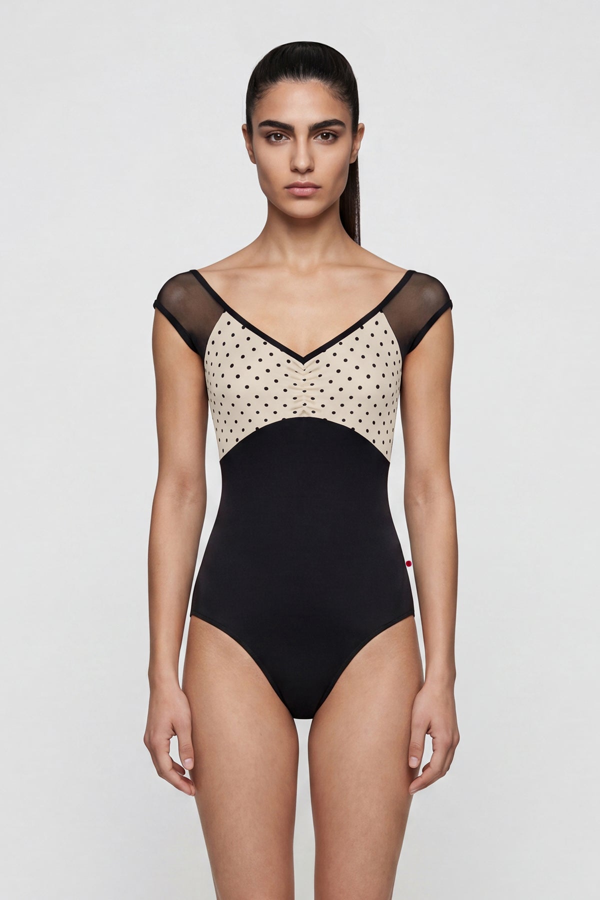 AI-generated model. Elli Mesh leotard, cream polka-dot ruched bust with sheer black mesh cap sleeves and V-neckline, black body.