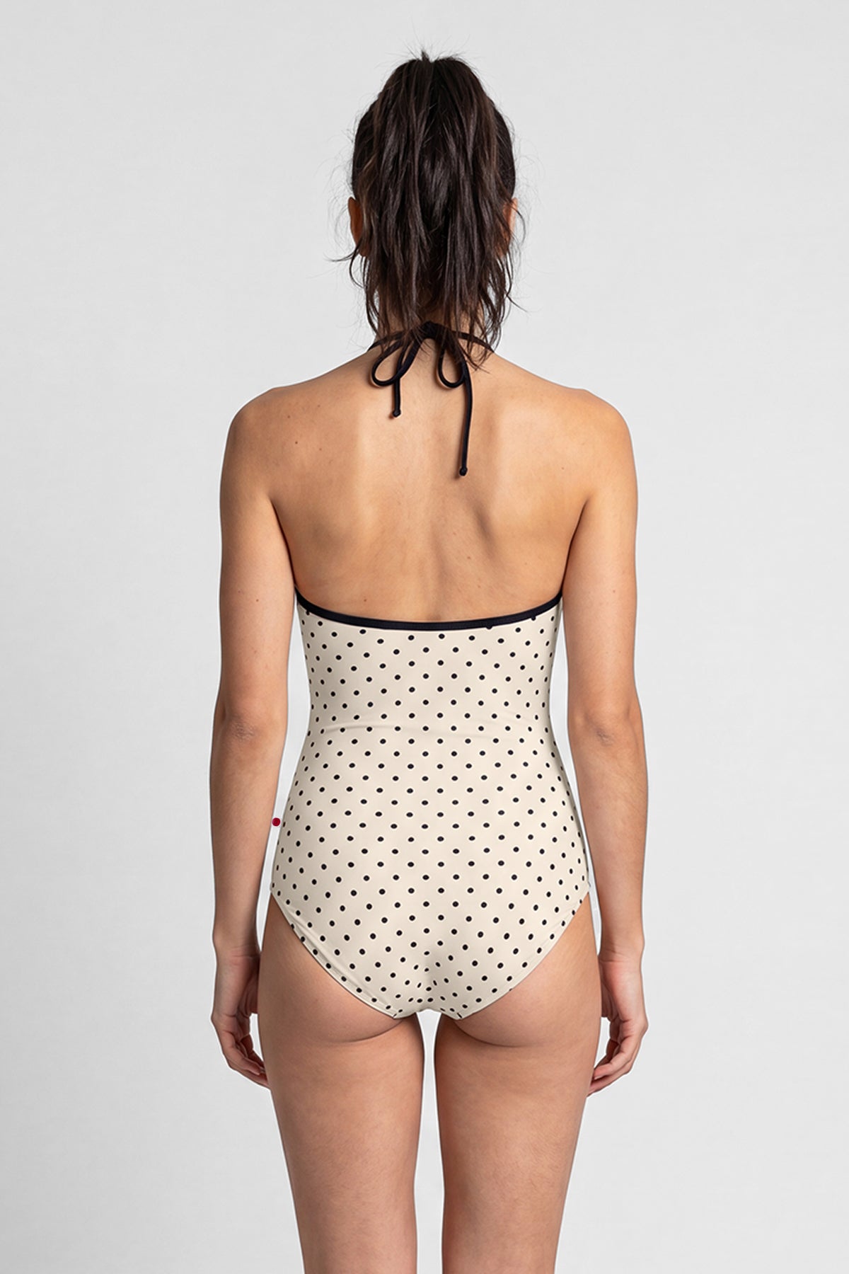 AI-generated model. Monique leotard, all-over cream polka-dot with a black halter neckline.