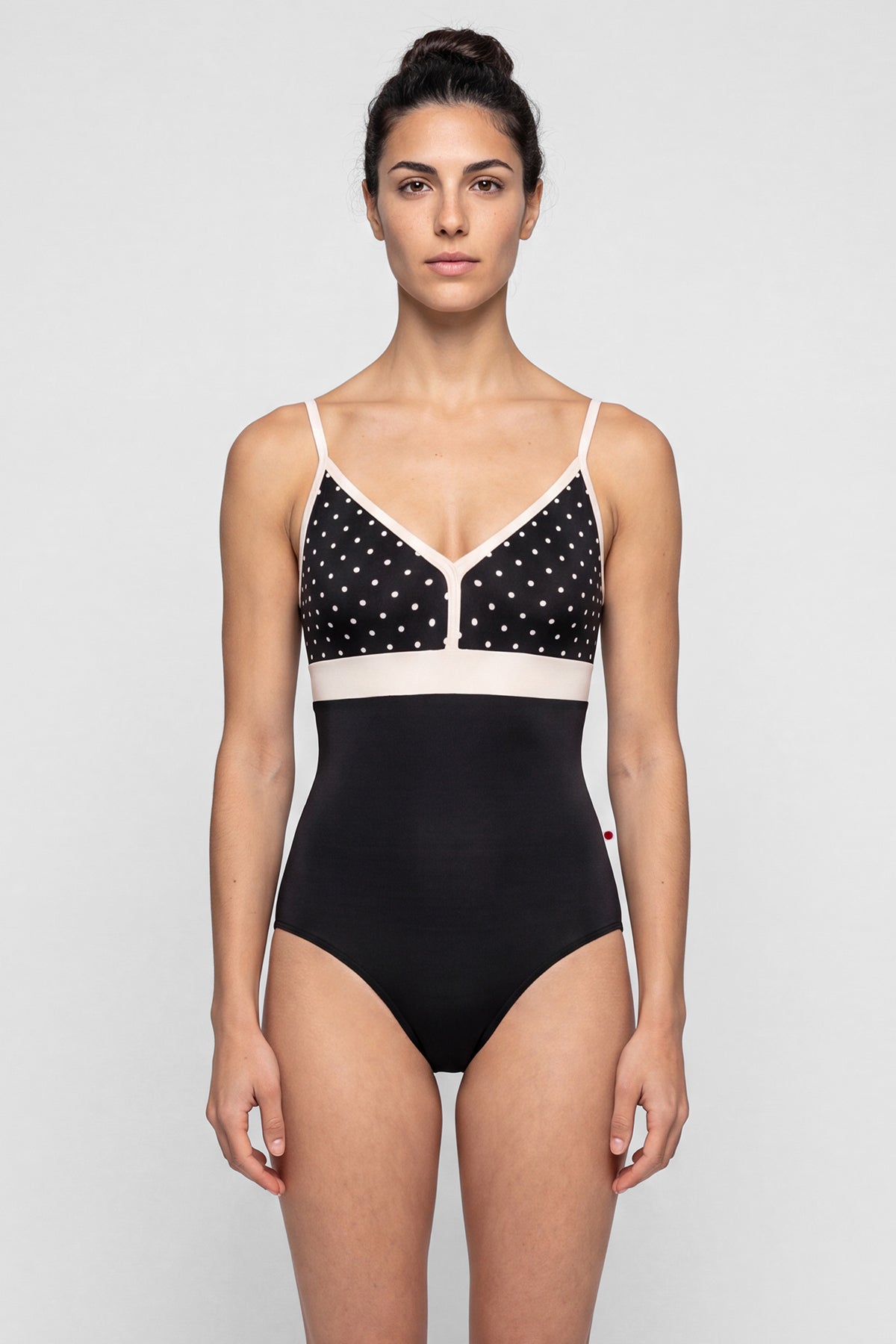AI-generated model. Zoe leotard, black T-Lunares polka-dot V-neck bust with blush straps and waistband, black body.