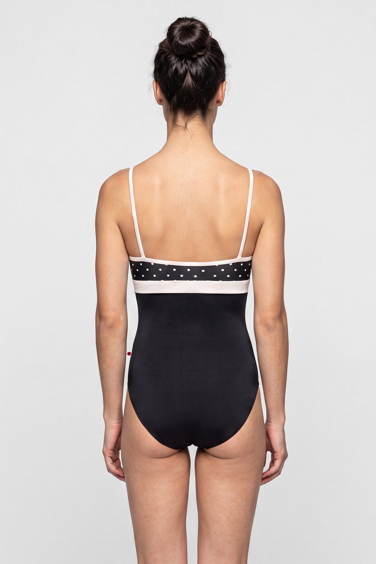 AI-generated model. Zoe leotard, black T-Lunares polka-dot V-neck bust with blush straps and waistband, black body.