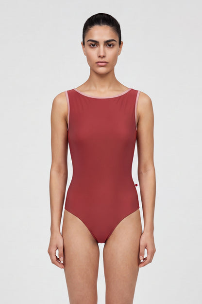 AI-generated model. Sofiane leotard, brick-red with a high boat neckline and pink strap trim.