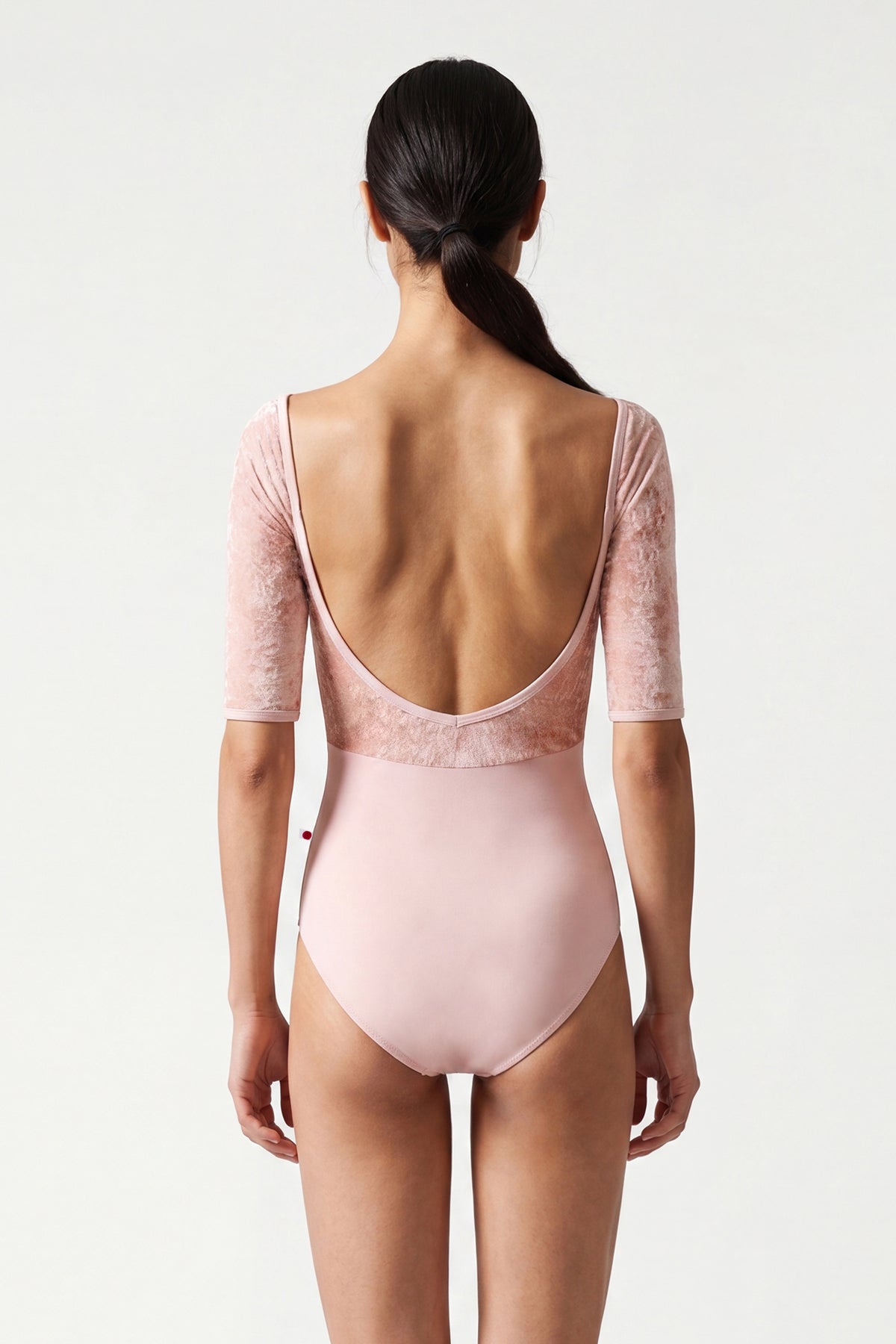 AI-generated model. Elli leotard, blush-pink with a crushed-velvet elbow-sleeve bodice and gathered V-neck.